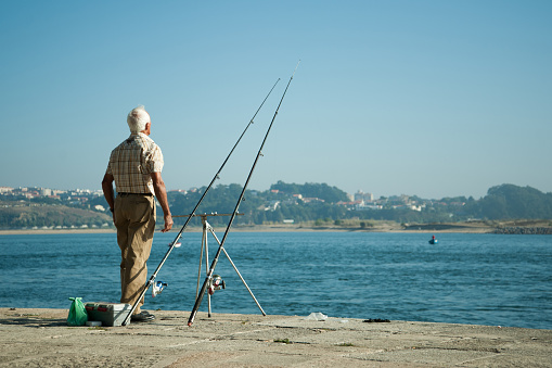 Old man with a fishing rod. Senior man fishing on the coast of the ocean in Portugal