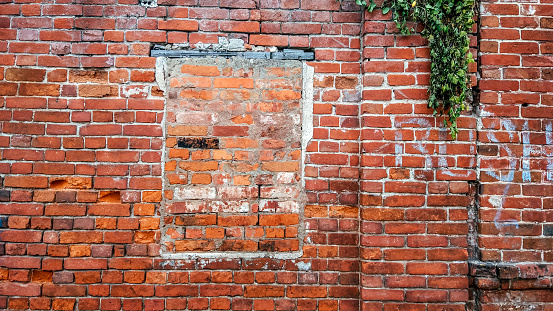 The brick wall, the window is bricked, old cement red brick in the summer in the city, a building that is abandoned.