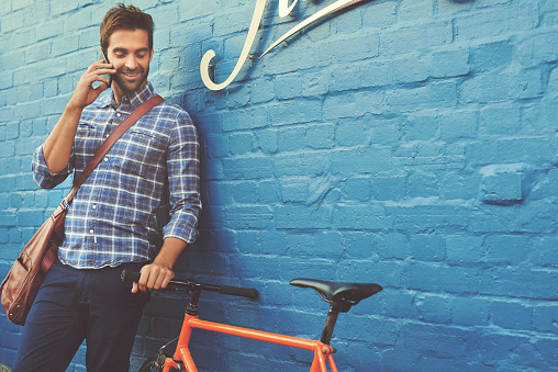 Shot of a handsome young man posing with his bicycle against a blue wall
