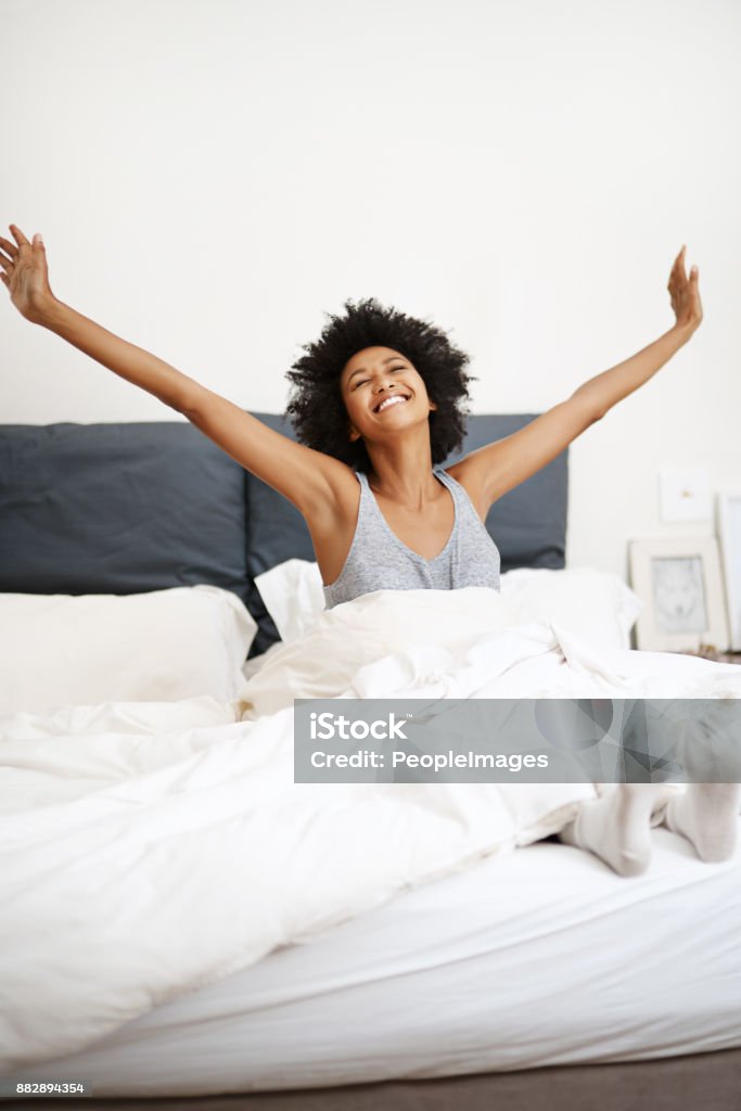 Making her morning a marvelous one Shot of a young woman stretching after waking up in her bed Waking up Stock Photo