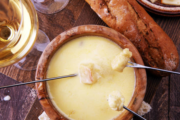 istock Gourmet Swiss fondue dinner on a winter evening with assorted cheeses on a board alongside a heated pot of cheese fondue with two forks dipping bread and white wine behind in a tavern or restaurant 882898000