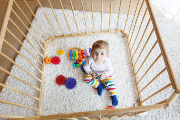 mooie babymeisje zit in de kinderbox. leuk schattig kind spelen met kleurrijke speelgoed - babybox stockfoto's en -beelden