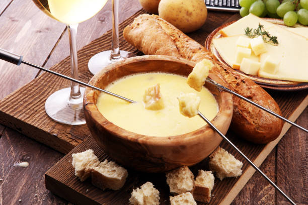 istock Gourmet Swiss fondue dinner on a winter evening with assorted cheeses on a board alongside a heated pot of cheese fondue with two forks dipping bread and white wine behind in a tavern or restaurant 882898446