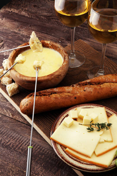 istock Gourmet Swiss fondue dinner on a winter evening with assorted cheeses on a board alongside a heated pot of cheese fondue with two forks dipping bread and white wine behind in a tavern or restaurant 882898580