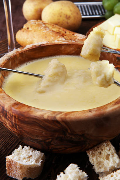 istock Gourmet Swiss fondue dinner on a winter evening with assorted cheeses on a board alongside a heated pot of cheese fondue with two forks dipping bread and white wine behind in a tavern or restaurant 882898702