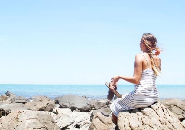 istock woman sitting on rocks at beautiful beach 882918280