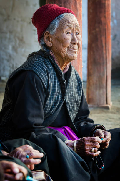 Tibetan senior woman with her buddhist prayer beads Phyang, India - July 14, 2015: Elderly Tibetan woman from Ladakh is praying with her buddhis prayer beads while she is watching and listening to traditional music during in a festival in the courtyard of Phyang Monastery, Ladakh. phyang monastery stock pictures, royalty-free photos & images