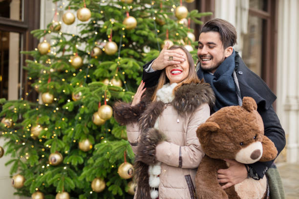 istock Handsome man surprising his girlfirend witha christmas teddy bear by covering her eyes 882928196