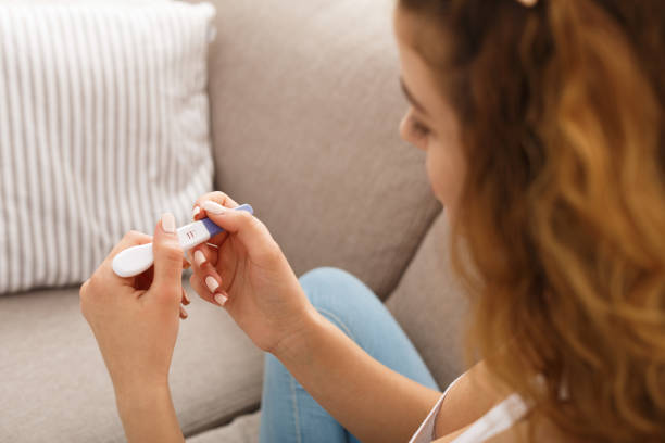 Worried girl reading the results of her pregnancy test Worried redhead girl checking her recent pregnancy test, sitting on beige couch at home family planning stock pictures, royalty-free photos & images