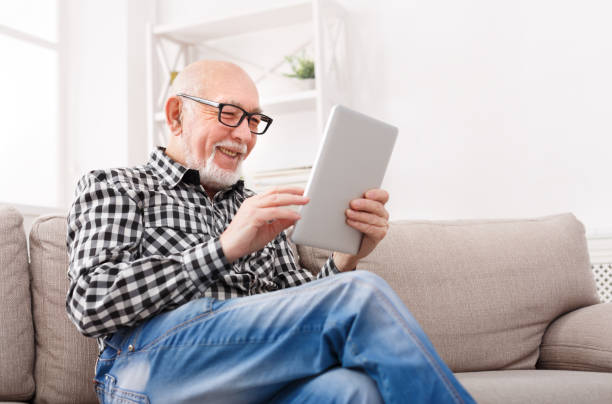 uomo anziano che legge notizie su tablet digitale - computer old men laptop foto e immagini stock