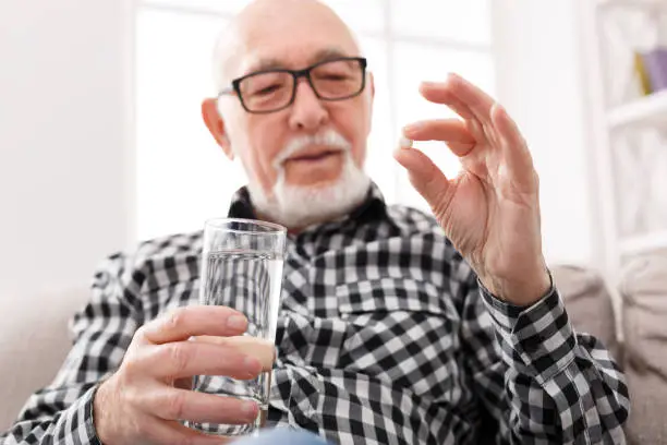 Photo of Old man having a glass of water and pills in hand