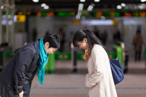 Two Japanese Businesswomen Bowing To Each Other At Station Two businesswomen are bowing to each other in front of station gates. bowing stock pictures, royalty-free photos & images