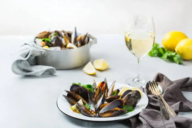 Still life, restaurant dinner. Shellfish mussels with lemon and green parsley with white wine. Seafood on a concrete table