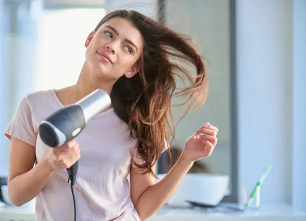 Cropped shot of a beautiful young woman blowdrying her hair in the bathroom at home