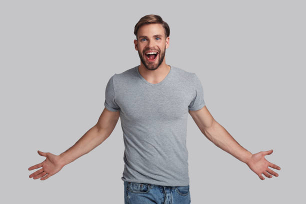 I am the champion! Charming young man keeping arms outstretched and shouting while standing against grey background arms outstretched stock pictures, royalty-free photos & images