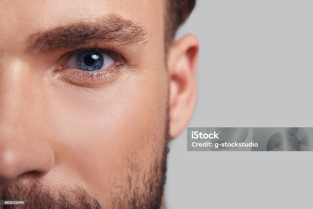 Looking deeply into your heart. Close up of good looking young man half face looking at camera while standing against grey background Men Stock Photo