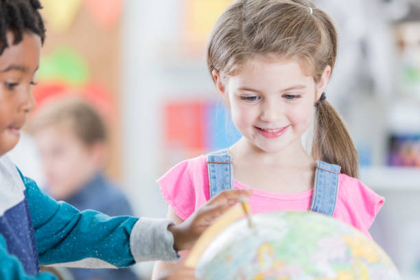 istock Cheerful little girl studies globe with friend 883044618