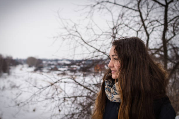 Pensive and romantic girl with beautiful long hair on the winter background looking away on the winter landscape