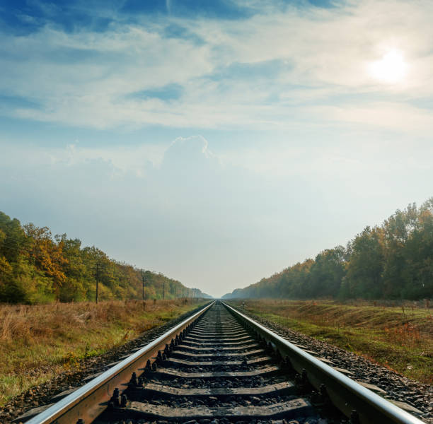 istock railroad closeup goes to horizon under cloudy sky with sun 883095598