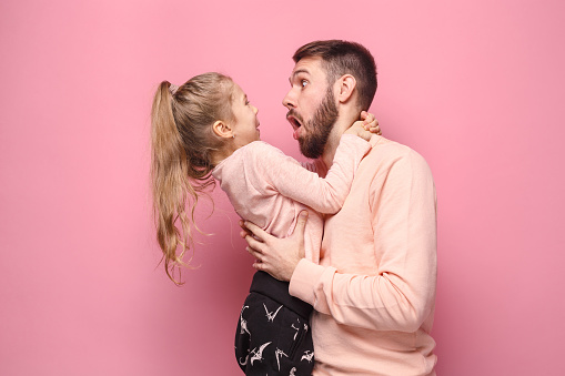 Young father with his baby daughter with surprised emotions at studio pink background