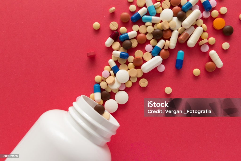 Group of assorted colorful tablets. Capsules spilling out of white bottle. Group of assorted colorful tablets. Capsules spilling out of white bottle. Red background. Line, way course concept. Vitamin Stock Photo