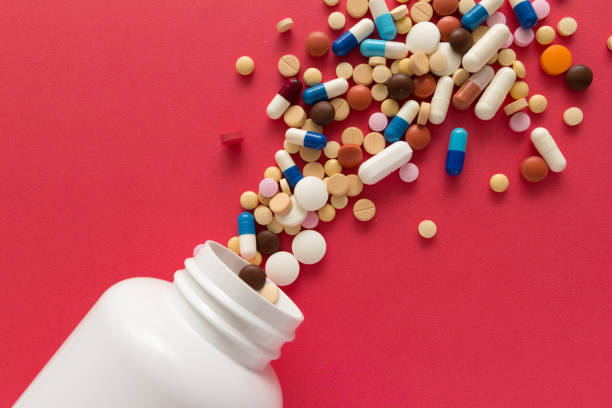 Group of assorted colorful tablets. Capsules spilling out of white bottle. Group of assorted colorful tablets. Capsules spilling out of white bottle. Red background. Line, way course concept. spilling photos stock pictures, royalty-free photos & images