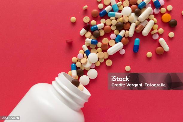 Group Of Assorted Colorful Tablets Capsules Spilling Out Of White Bottle Stock Photo - Download Image Now