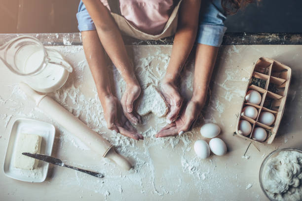 Mom with daughter on kitchen. Cropped image of attractive young woman and her little cute daughter are cooking on kitchen. Having fun together while making cakes and cookies. Top view of mom with daughter making dough heart. flour photos stock pictures, royalty-free photos & images