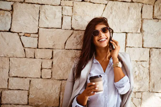 Happy brunette businesswoman with suit talking on the phone and drinking coffee in Mediterranean city