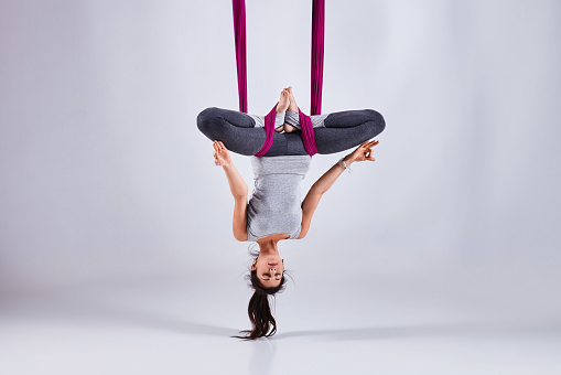 Young woman practices aerial different inversion antigravity yoga with a hammock in a white studio. Concept of a mental and physical health and harmony living
