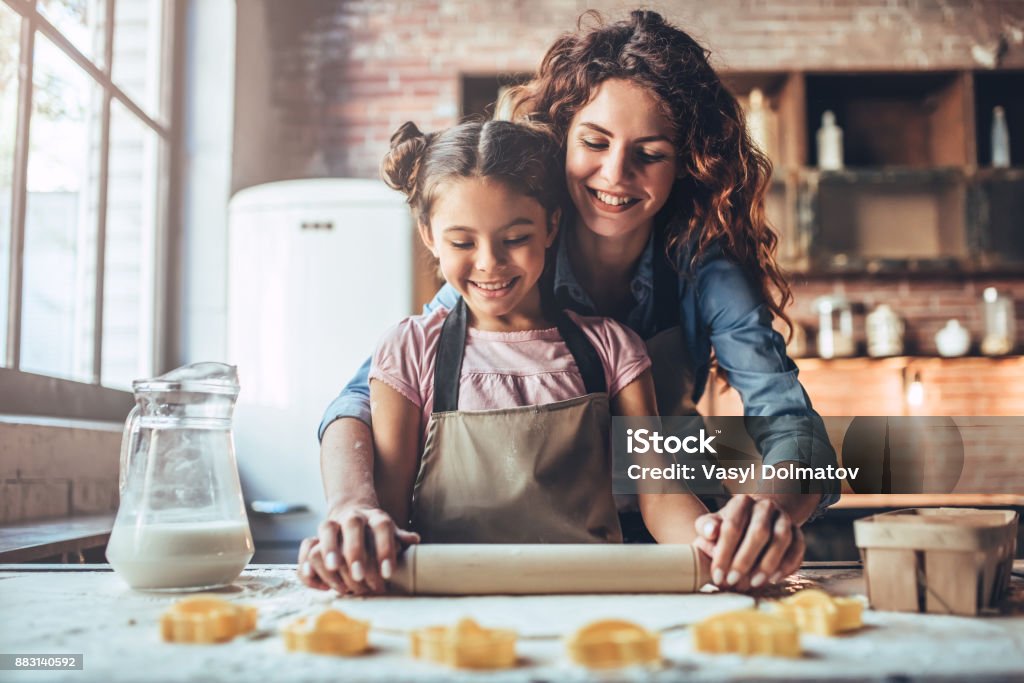 Mom with daughter on kitchen. Attractive young woman and her little cute daughter are cooking on kitchen. Having fun together while making cakes and cookies. Cooking Stock Photo