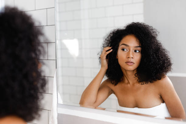 istock Young woman standing in bathroom, holding her curly hair while looking at a mirror 883147364