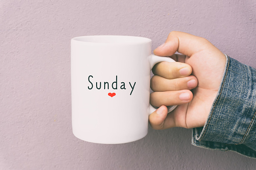 Woman Hand Holding a Cup of Coffee With Text Sunday.