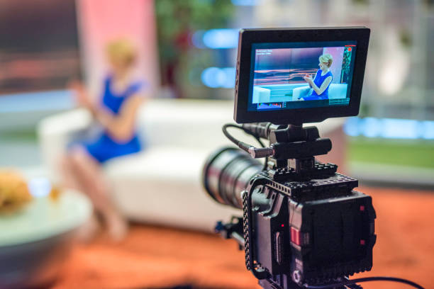 Talk show host In foreground female talk show host on camera display, in blurred background show host in blue dress sitting on a sofa and clapping, copy space. television host stock pictures, royalty-free photos & images