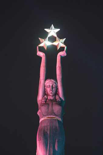 Riga, Latvia - November 20, 2017: The Freedom Monument of Latvia in the nighttime amidst the festival “Staro Riga” in which popular spots in Riga are getting lit by different colored lights. The monument is of a woman called Milda who's clad in copper. The 3 stars held in her hand symbolizes 3 regions of Latvia. The author of the monument is Karlis Zale (1888 – 1942) and Ernest Stalberg (1883 – 1958).
