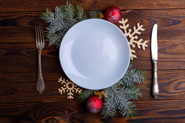 istock On the table an empty plate, a knife and a fork are decorated with branches of a Christmas tree. View from above. 883170472