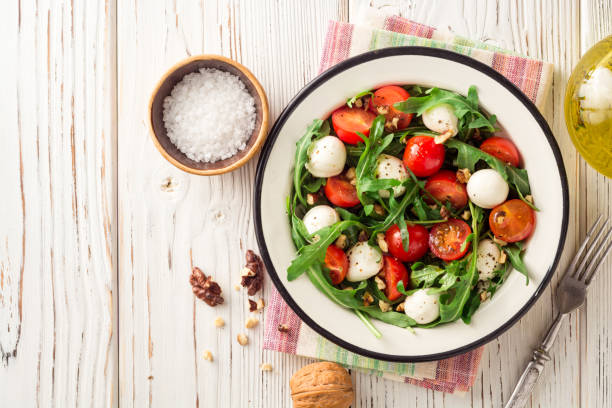istock Fresh salad with arugula, cherry tomatoes, mozzarella cheese and walnuts on white wooden background. 883181724