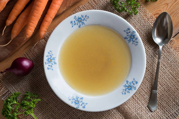 istock Chicken stock in a white plate, with vegetables in the background 883182048
