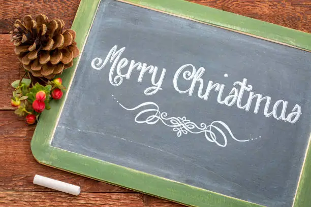 Merry Christmas greeting card - white chalk text  on a vintage slate blackboard with a pine cone