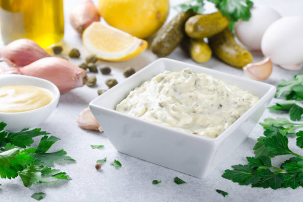 Traditional french sauce remoulade in a white bowl with ingredie Homemade traditional french sauce remoulade in a white bowl with ingredients, lemon, eggs, shallot onion, pickles, parsley, mustard on a light stone background. Horizontal dipping photos stock pictures, royalty-free photos & images