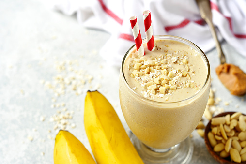 Banana peanut butter smoothie with oats and cinnamon in a glass on a light slate,stone or concrete background.