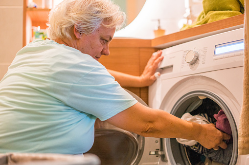 Side view senior women taking wet laundry from washing machine