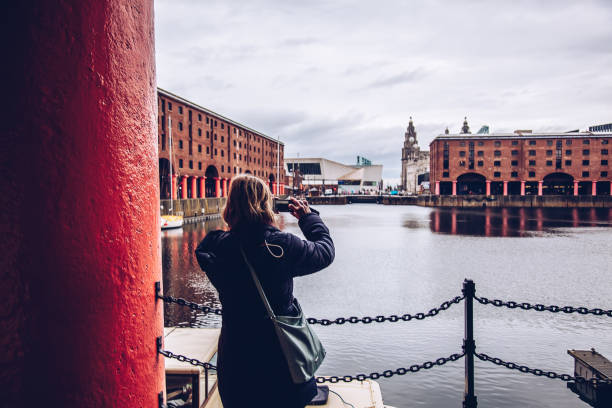 Tourist in the Albert Dock, Liverpool Liverpool, UK - August 17, 2016: View across the Albert Dock, Liverpool show the city skyline. A boat can be seen moored in the dock. There is one woman who takes photos with her mobile phone. liverpool one stock pictures, royalty-free photos & images