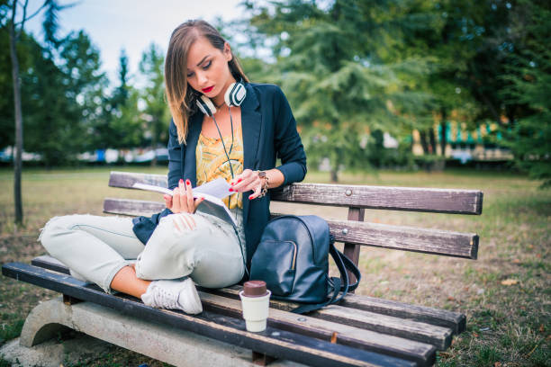 istock Woman with a headphones sitting on a bench and reading a book 883377014