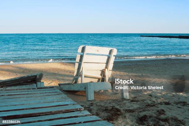 One Lonely Old White Vintage Wooden Sun Lounger Standing At The Abandoned Beach After The End Of A Summen Season In The Evening Sunlight Stock Photo - Download Image Now
