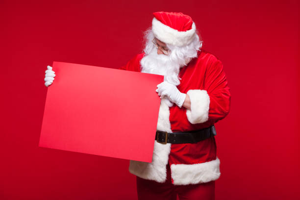 istock Santa Claus pointing in blank advertisement banner isolated on red background with copy space red leaf 883559470