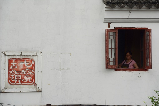 Woman at a window in the picturesque Qibao, an old water town in Shanghai. \n