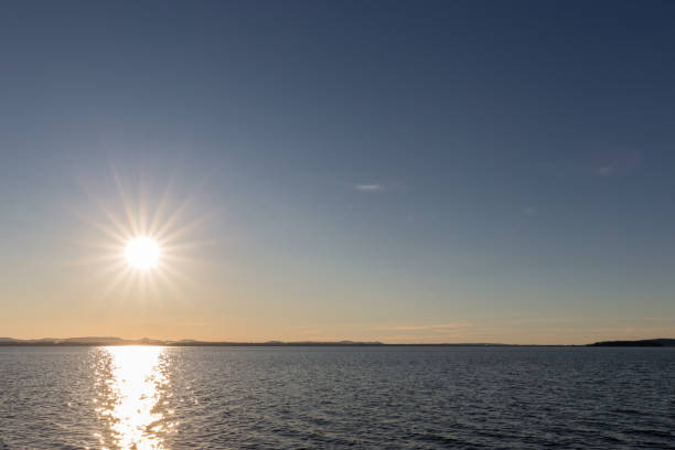 istock Sunset on a lake, with star shaped sun and almost empty blue sky 883622932