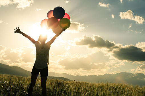 Cheering young asian woman on grassland with colored balloons