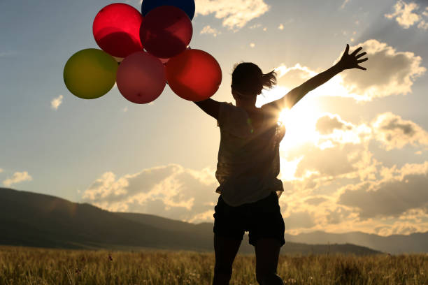 istock Cheering young woman jumping on grassland with colored balloons 883660938